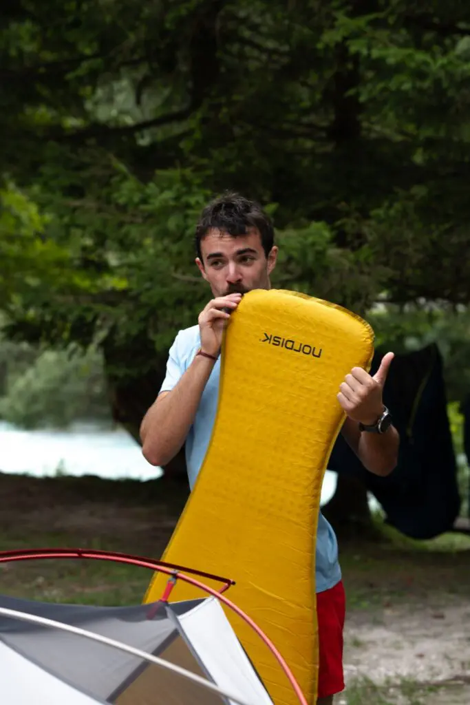 man inflating a yellow sleeping mat while camping