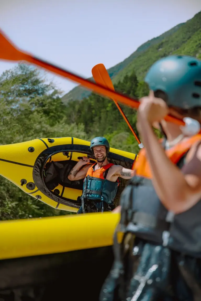man carrying yellow packraft with paddle on shoulder