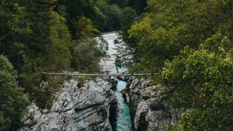 person on a suspension bridge over a turquoise river in a gorge