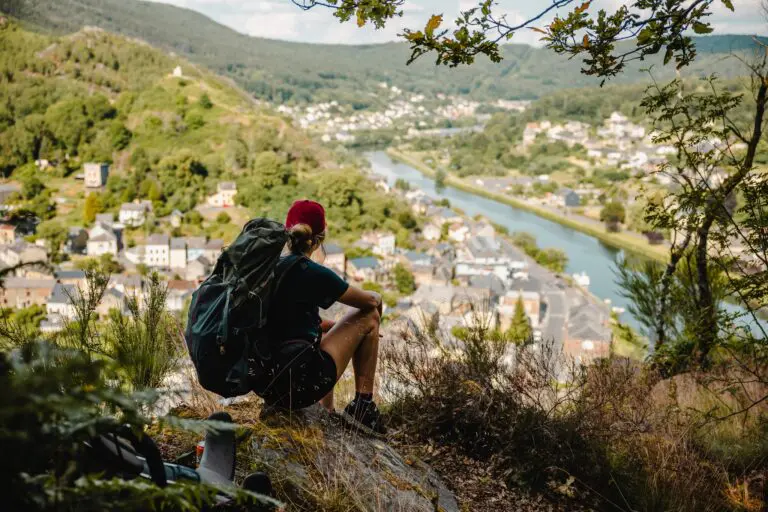Wandelaar met rugzak kijkt uit over een dorp en rivier in de Ardennen