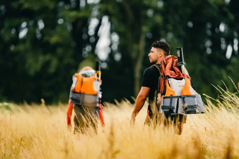 two people hiking through tall grass with packrafts