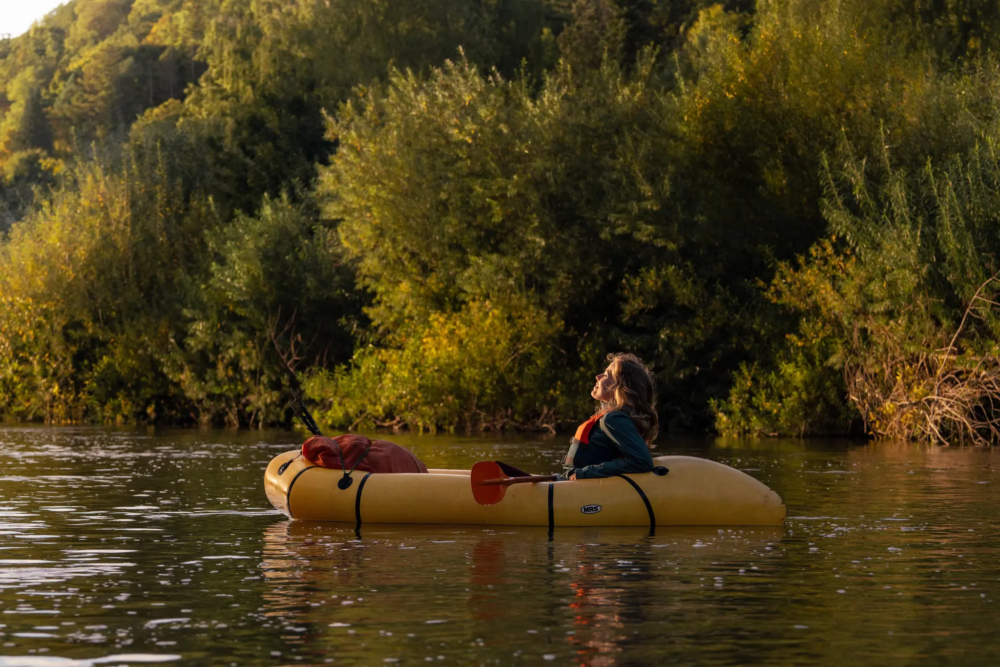 Frau im Packraft auf einem Fluss bei Sonnenuntergang