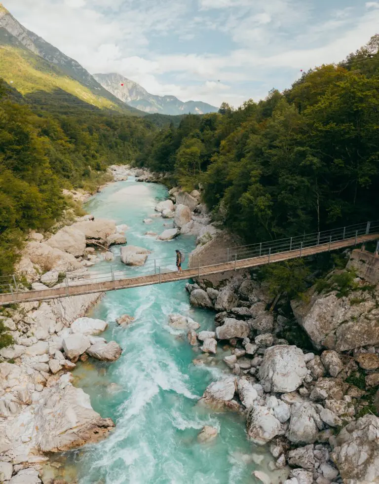 persoon op een hangbrug boven een turquoise rivier in Slovenië