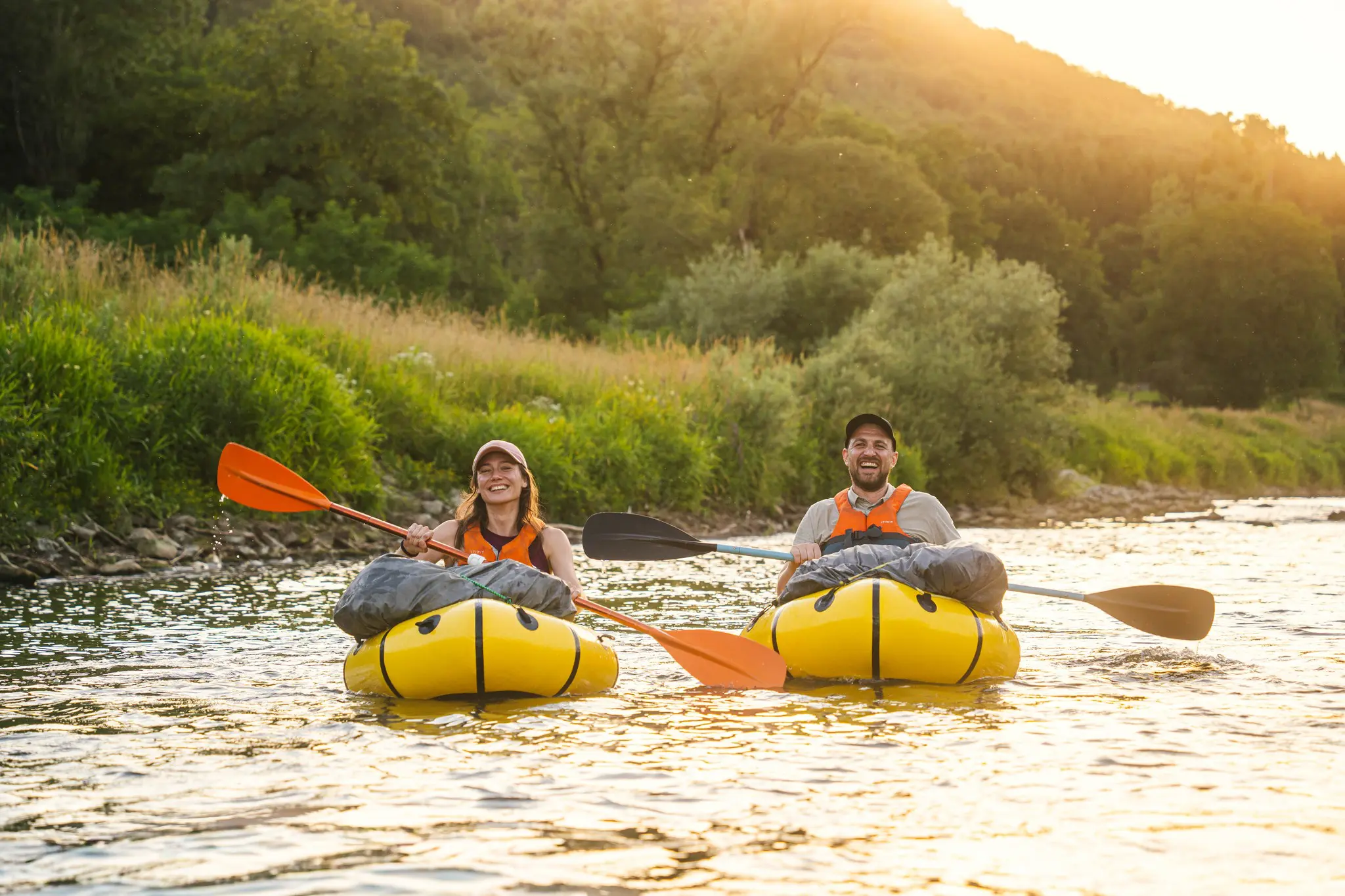 zwei Menschen beim Packrafting auf einem Fluss bei Sonnenuntergang im Müllerthal
