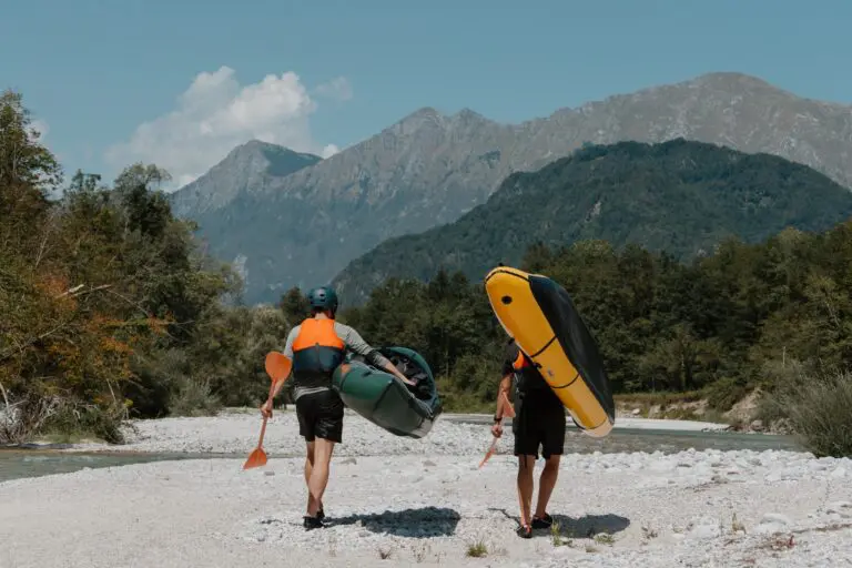two people carrying packrafts and paddles along a river in Slovenia