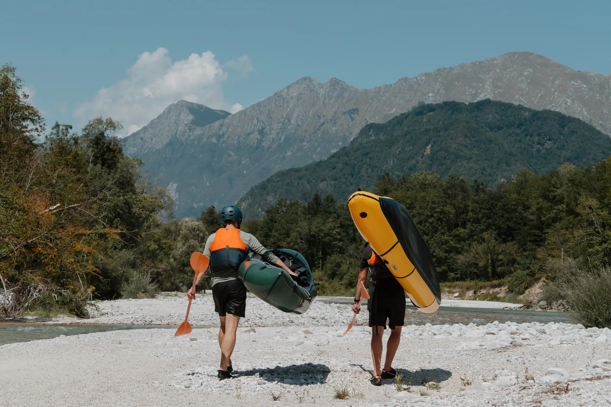 two people carrying packrafts and paddles along a river in Slovenia