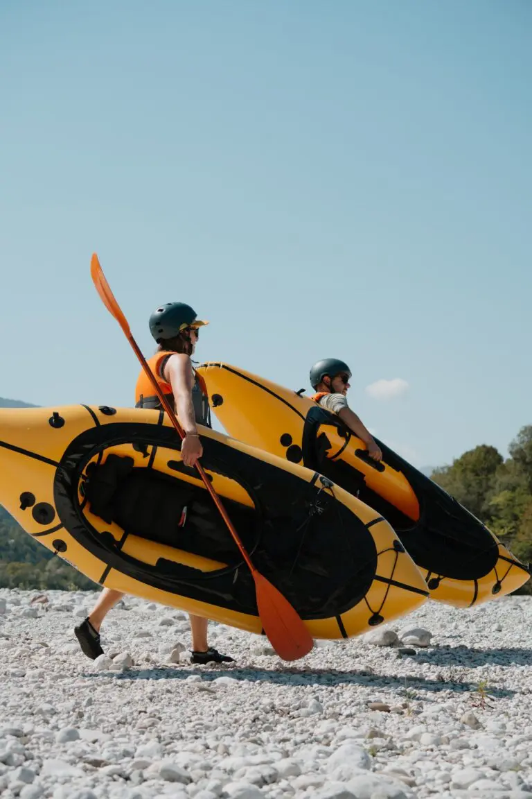 deux personnes portant des packrafts jaunes et des pagaies sur une berge rocheuse