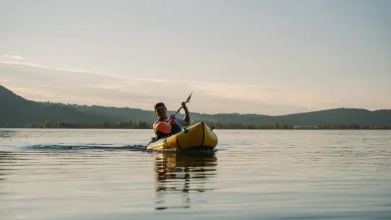 man paddling yellow packraft on a lake at sunset