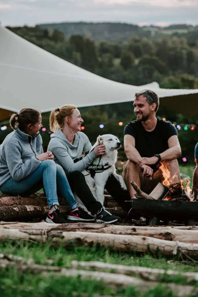 trois personnes et un chien assis autour d’un feu de camp