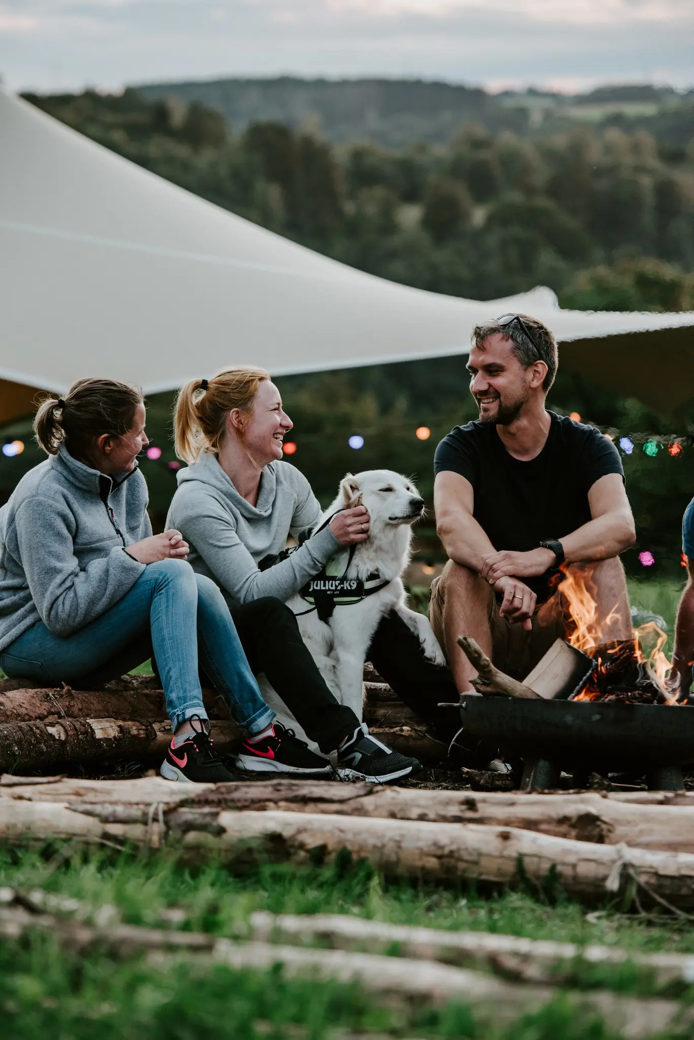 trois personnes et un chien assis autour d’un feu de camp