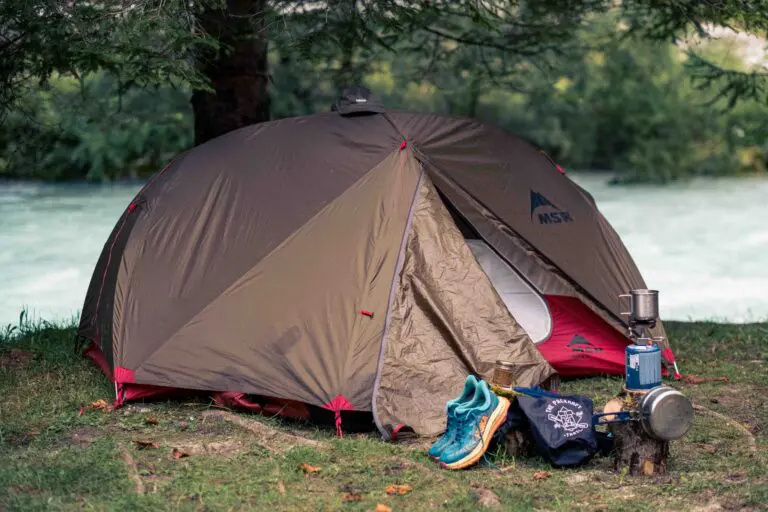 camping tent by river with hiking shoes and cooking gear