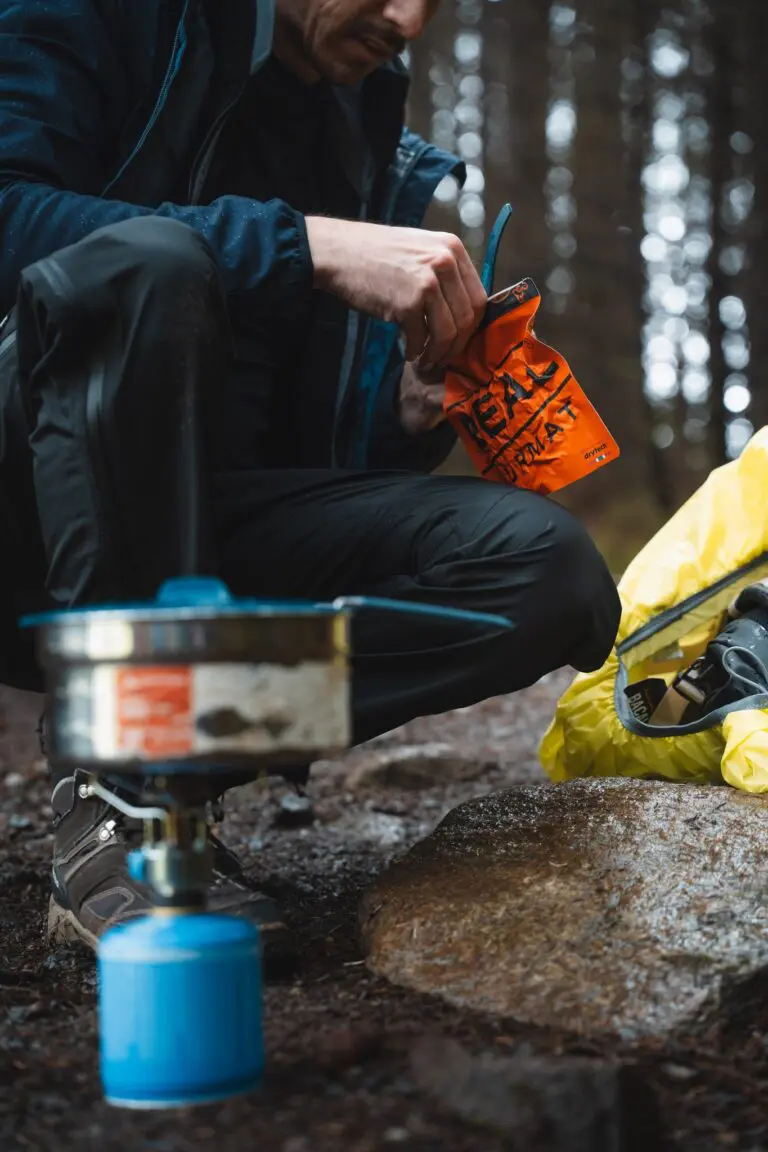 person preparing a meal with a camping stove in a forest